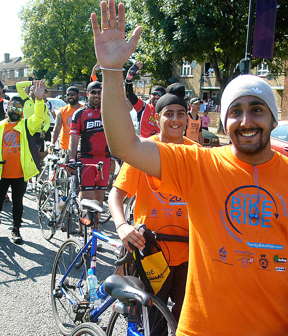 A group of male Southall residents with bikes, waving and waiting to start a charity bike ride.